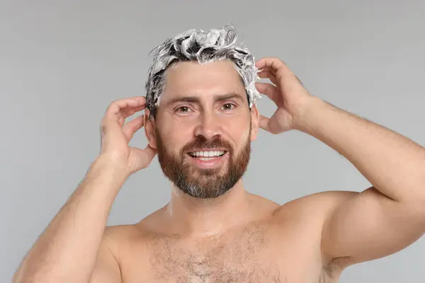 stock image Happy man washing his hair with shampoo on grey background