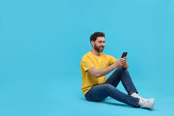 stock image Smiling man with smartphone on light blue background. Space for text