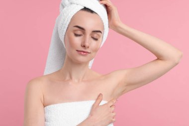 Güzel bir kadın pembe arka planda pürüzsüz, temiz bir ciltle koltukaltı gösteriyor.