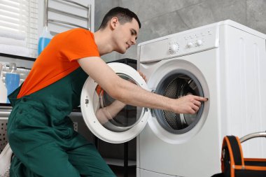 Gülümseyen tesisatçı banyoda çamaşır makinesini tamir ediyor.