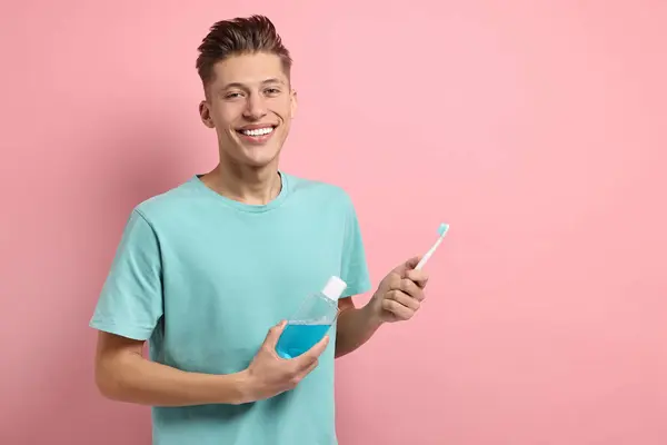 ピンクの背景にマウスウォッシュと歯ブラシを持つ若者 テキストのためのスペース — ストック写真