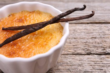 Lezzetli creme brulee kasede ve ahşap masada vanilya kabukları, yakın plan