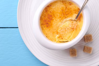 Lezzetli creme brulee kasede, şeker küpleri ve kaşık açık mavi ahşap masa, üst görünüm
