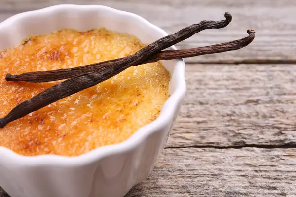 Lezzetli creme brulee kasede ve ahşap masada vanilya kabukları, yakın plan