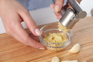 Tahta masada basınla sarımsak sıkan kadın, yakın plan.