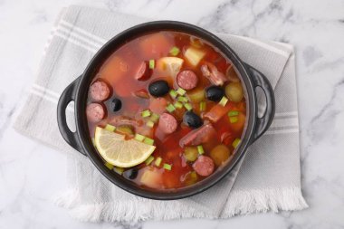 Meat solyanka soup with thin dry smoked sausages in bowl on white marble table, top view clipart