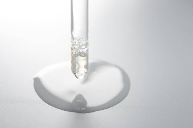 Açık gri arka planda pipetten damlayan nemlendirici serum, yakın plan. Metin için boşluk