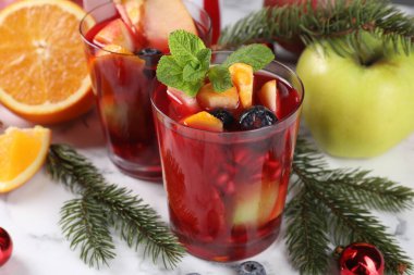 Aromatik Sangria içeceği bardaklarda, malzemelerde ve beyaz mermer masada Noel dekorunda.