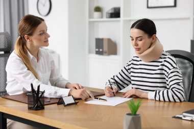 Yaralı kadın avukatın ofisinde belge imzalıyor.