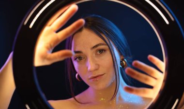 Koyu arkaplanda güzel bir kadının portresi neon ışıklarıyla, yüzük lambasının arkasından.