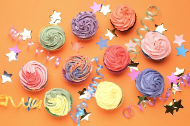 Parlak kremalı enfes kekler ve turuncu arka planda parti dekorasyonu, düz yatış.