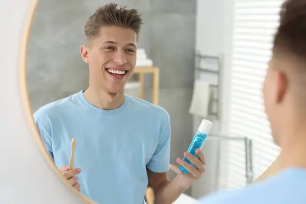 バスルームの鏡の近くにマウスウォッシュと歯ブラシを持つ若い男 — ストック写真