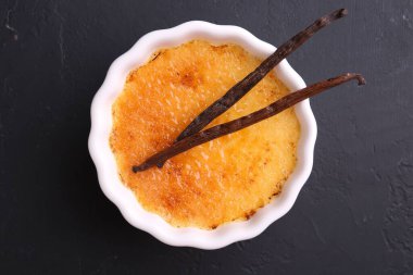 Lezzetli creme brulee kasede ve vanilyalı kaplar koyu gri desenli masa, üst manzara