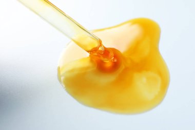 Açık gri arkaplanda pipetten damlayan nemlendirici serum, yakın plan