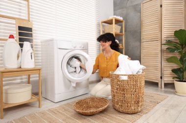 Çamaşır makinesine çamaşır koyan mutlu bir kadın.