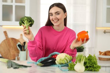 Mutfaktaki açık mermer masada elinde sebze ve ip torbası olan bir kadın.