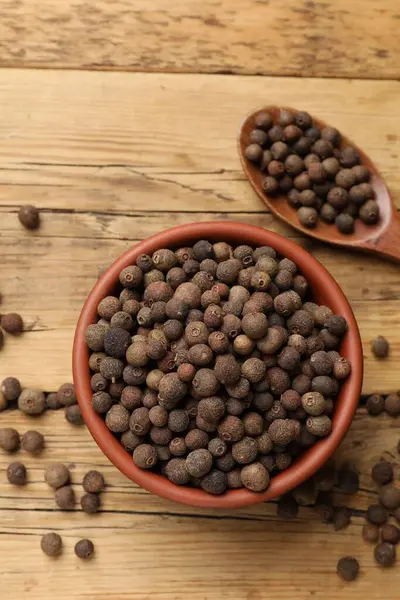 Aromatik biber taneleri kasede ve kaşıklar ahşap masada, üst tarafta.