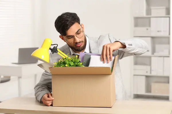 Unemployment problem. Frustrated man with box of personal belongings at desk in office
