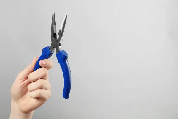 Woman with needle nose pliers on grey background, closeup. Space for text