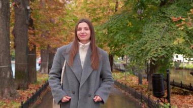 Gri ceketli çekici bir kadın yağmurdan sonra sonbahar parkında yürüyor. Kamera geri gidiyor