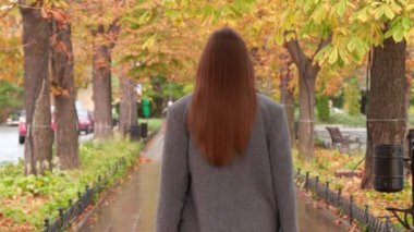 Güz parkında şık gri ceketli çekici bir kadın yürüyor. Kamera onun peşinden gidiyor.
