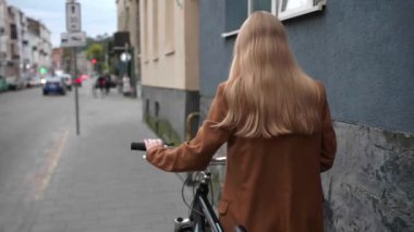 Bisikletli genç bir kadın sokakta yürüyor, arka manzaralı. Kamera ondan sonra hareket ediyor, yavaş çekim etkisi