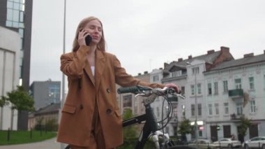 Dışarıda bisikletli genç bir kadın cep telefonuyla konuşuyor.