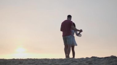 Gün batımında sahilde dans eden güzel bir çift, alçak açılı bir manzara. Yavaş çekim etkisi