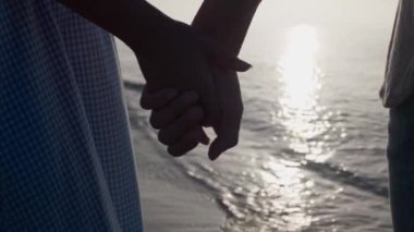 Gün batımında deniz kenarında el ele tutuşan çift, yakın çekim. Yavaş çekim etkisi