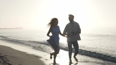 Gün batımında kumsalda koşan mutlu çift, yavaş çekim etkisi. Kamera izleme