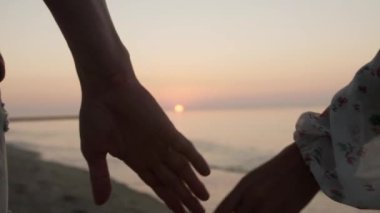 Gün batımında deniz kenarında el ele tutuşan çift, yakın çekim.