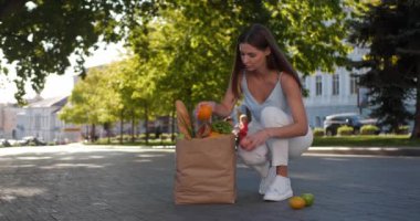 Çekici genç bir kadın sokakta düşmüş meyveleri kağıt torbaya dolduruyor, düşük açılı.