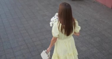 Çiçek buketi olan güzel genç bir kadın caddede yürüyor. Kamera kızdan sonra hareket ediyor