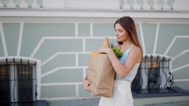 ストリートを歩く食料品の紙袋を持つ魅力的な若い女性 ゆっくり動き カメラトラック — ストック動画