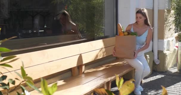 有魅力的年轻女子 提着纸袋食品 坐在长椅上 在户外休息 — 图库视频影像