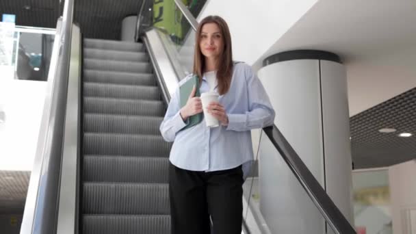 快乐的年轻女人 带着平板电脑和外卖咖啡在自动扶梯上移动 视角低 相机向后移动 慢动作效果 — 图库视频影像