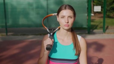 Şık spor kıyafetleri içinde tenis kortunda raketle yürüyen güzel bir kadın. Kamera geri gidiyor
