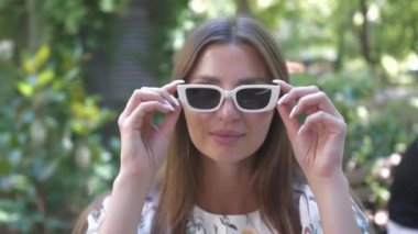 Güzel kadın güneş gözlüğünü çıkarıyor ve dışarıda kameraya gülümsüyor.