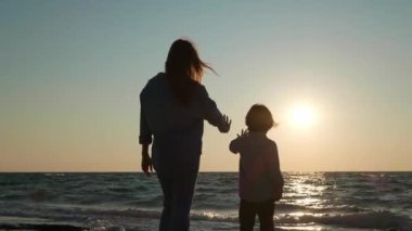 Anne ve oğlu gün batımında, deniz kenarında birlikte vakit geçiriyorlar.