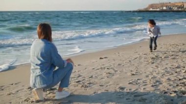 Küçük çocuk plajda annesine sarılmak için koşuyor. Genç bir kadın oğlunu yakalayıp etrafında döndürüyor.