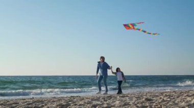 Anne ve oğlu deniz kenarında uçurtmayla oynuyorlar. Kamera sola hareket ediyor