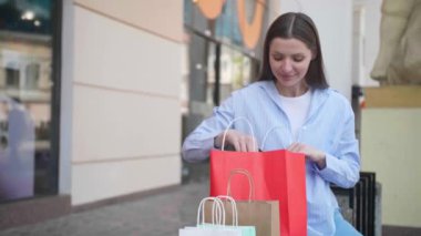 Dışarıda alışveriş yaptıktan sonra çantalarıyla güzel bir genç kadın, ağır çekim etkisi