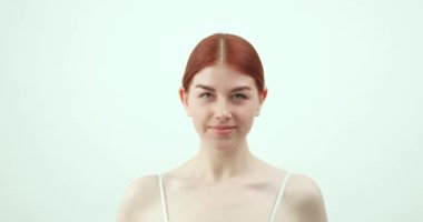 Kızıl saçlı, yeşil gözlü, beyaz arka planda kameraya bakan güzel bir kız.