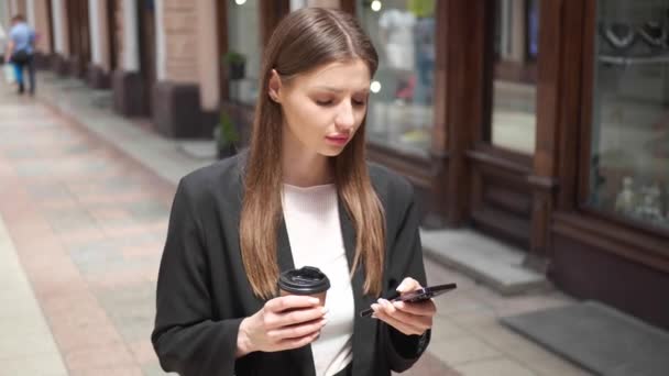 Mulher Bonita Com Bebida Takeaway Usando Telefone Celular Enquanto Caminhava — Vídeo de Stock