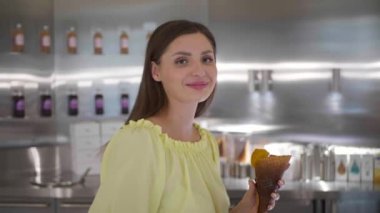 Lezzetli dondurması olan genç ve güzel bir kadın kafede yürüyor. Kamera geri gidiyor