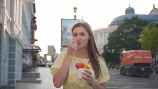美丽的年轻女子在城市里散步时吃冰淇淋 相机向后移动 慢动作效果 — 图库视频影像