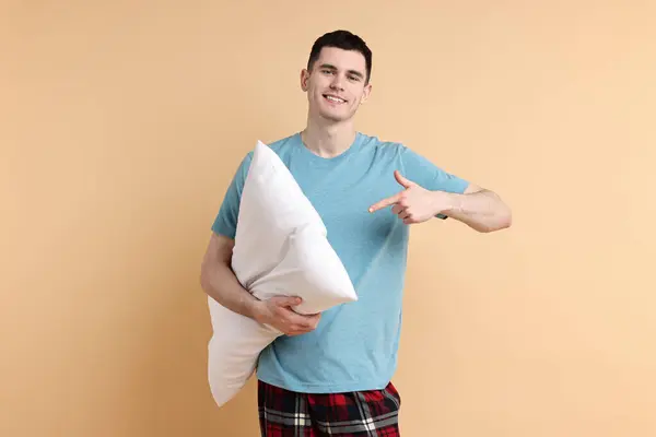 stock image Happy man in pyjama holding pillow on beige background