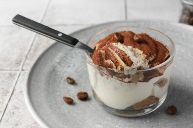 Bardakta nefis tiramisu, kahve çekirdekleri ve kaşık ışıklı masa, yakın plan.