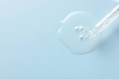 Açık gri arka planda pipetten damlayan nemlendirici serum, üst manzara. Metin için boşluk