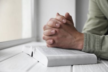 Religion. Christian man praying over Bible at white wooden the table, closeup clipart